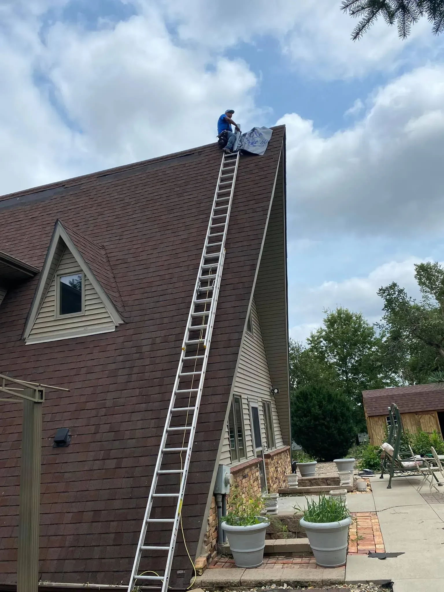 A man is sitting on top of a ladder on the roof of a house.