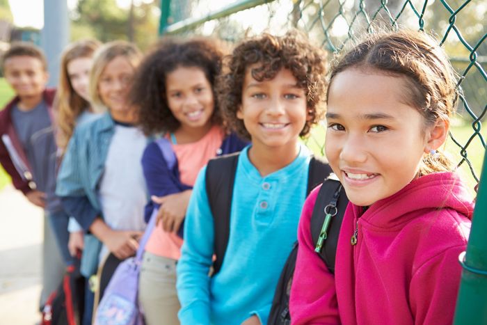 a girl in a pink hoodie stands in front of a chain link fence