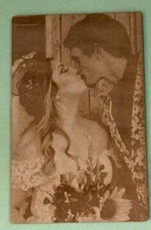 Wedding photo: Couple kissing, bride in veil, holding flowers, against a wooden background.