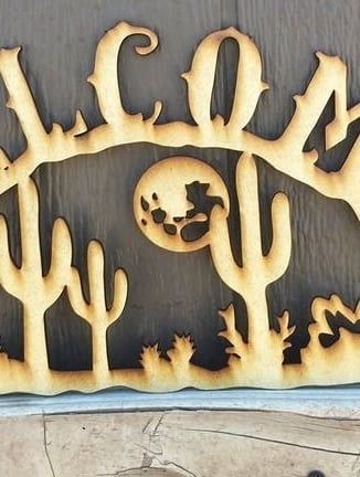 Wooden cutout of a desert scene with cacti, a moon, and the word 