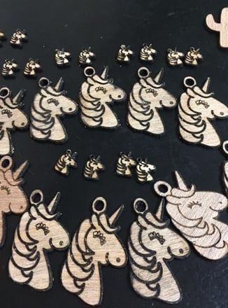 Wooden unicorn head cutouts, varying sizes, arranged on a dark surface. Burned details, eyes closed, some with eyelets.
