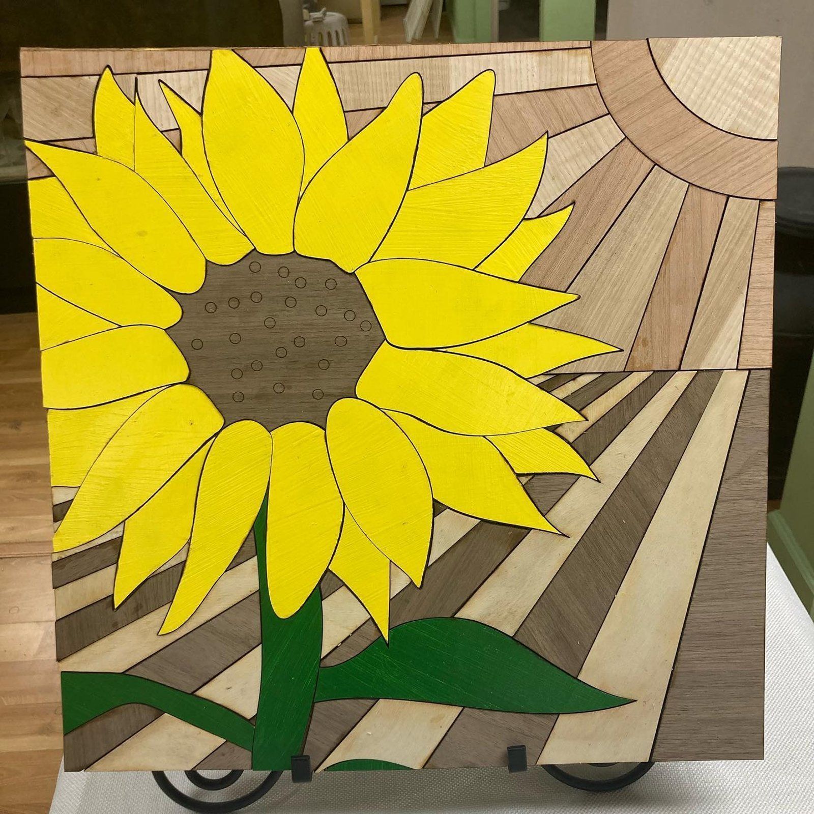 Wooden art piece of a sunflower, painted yellow, brown, and green with sun rays in the background.