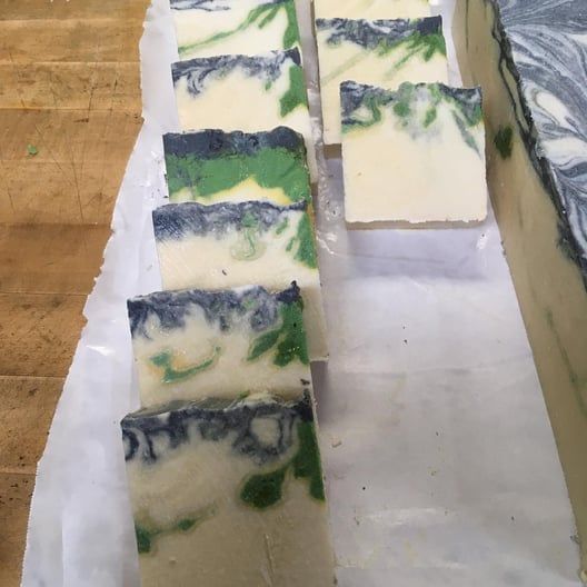 Slices of handmade soap with green, white, and gray swirls on parchment paper.