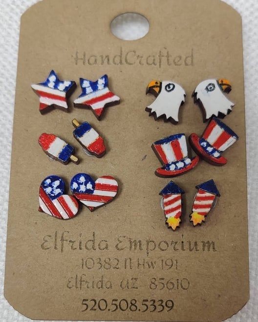 Earrings for sale: patriotic star, heart, eagle, firework, and hat designs, red, white, and blue, on a brown card.