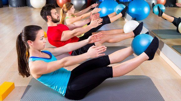een groep mensen doet oefeningen met pilatesballen in een sportschool.