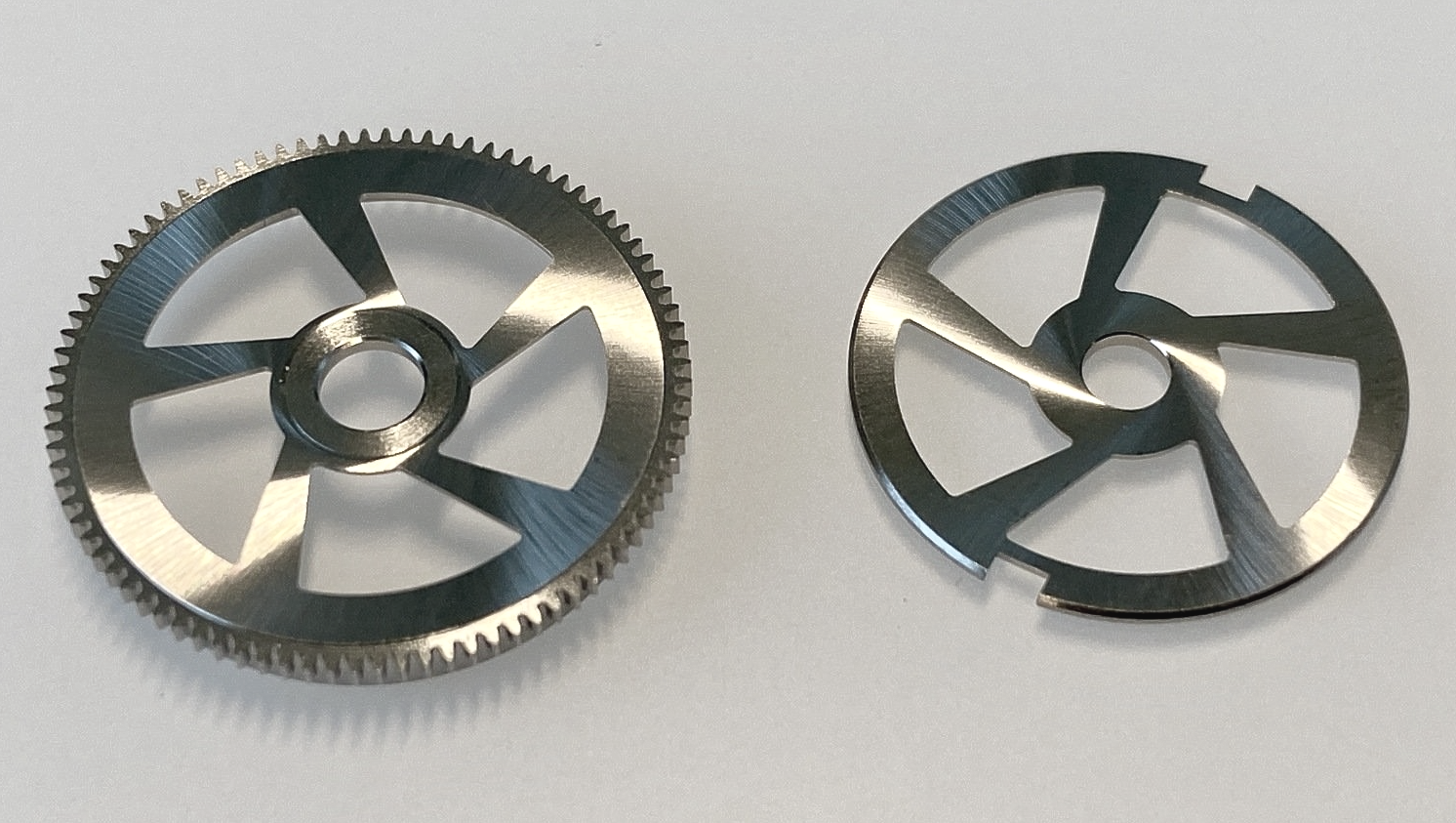 Two stainless steel gears on a white surface.