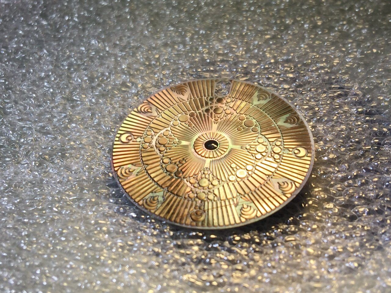 A gold plated button on a silver surface.