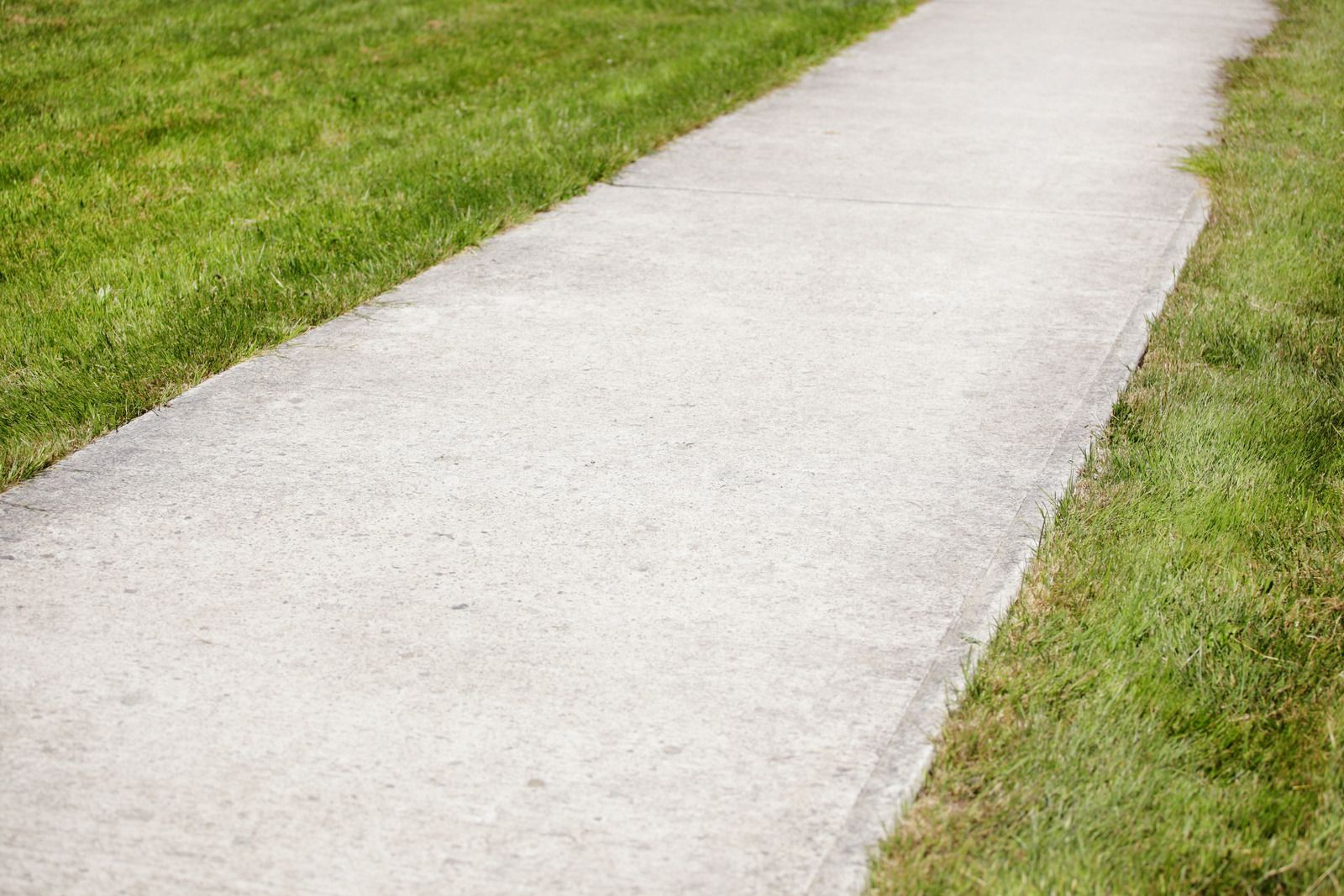 Concrete walkway bordered by green grass.
