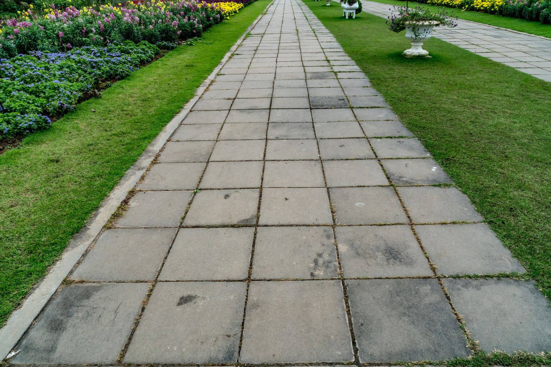 A brick walkway in a park with flowers on the side