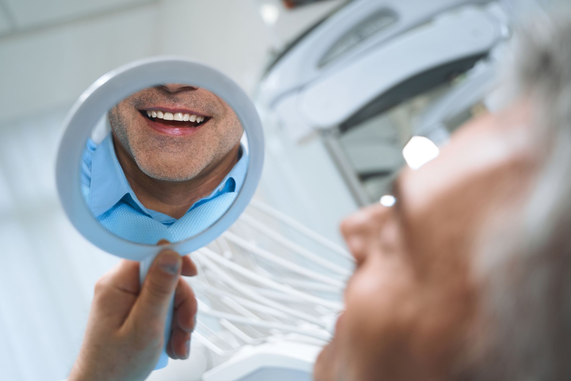 Happy man checking his smile in a mirror after getting dental implants at a modern clinic.