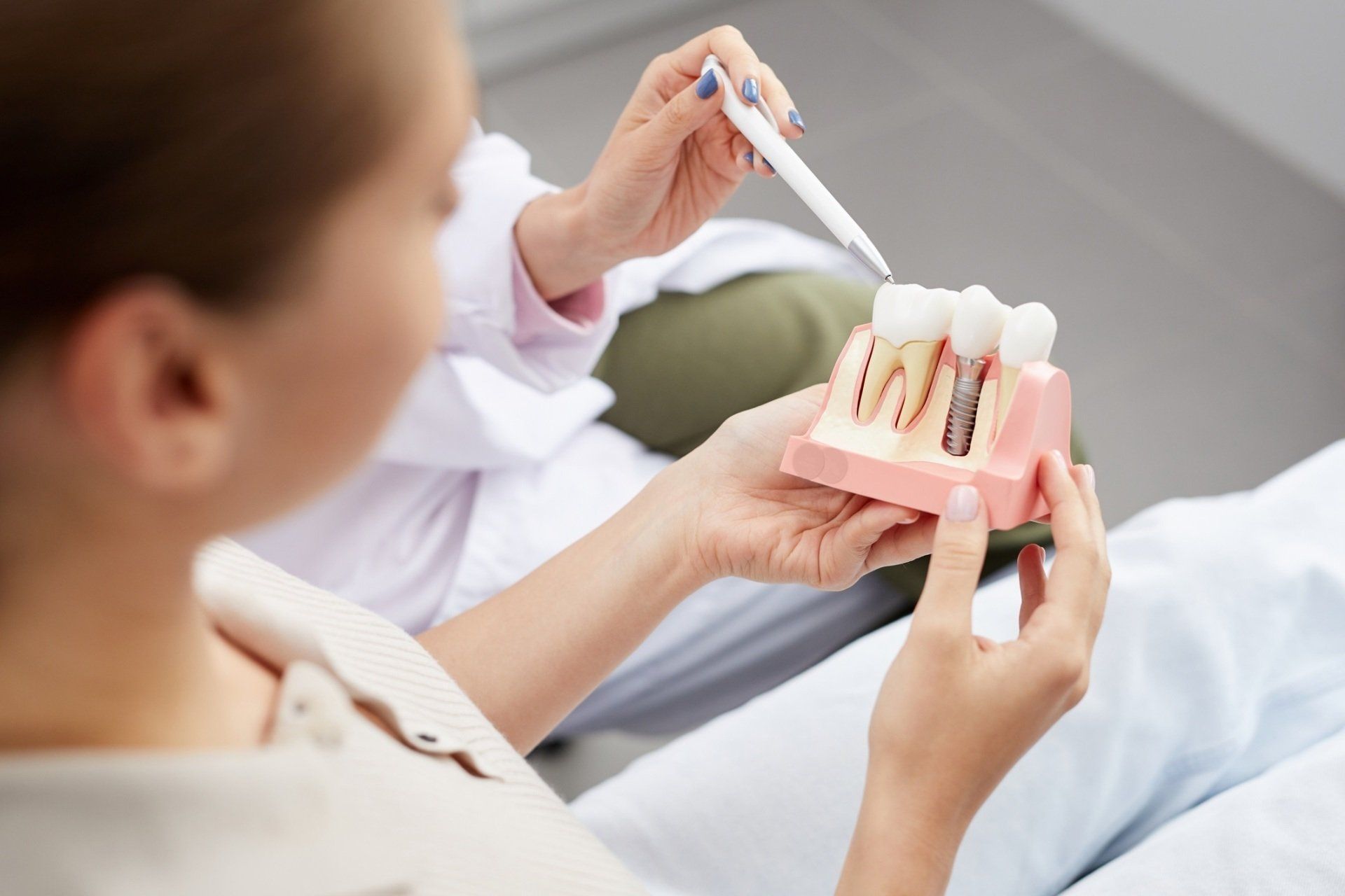 Dentist using pen to explain dental implant model to patient.