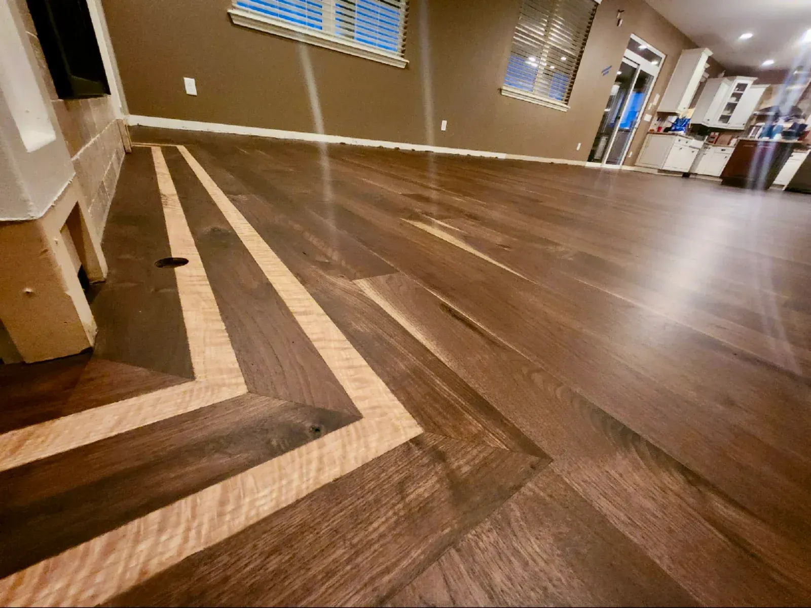 Hardwood floor with light border and dark planks in a room with windows and cabinets.