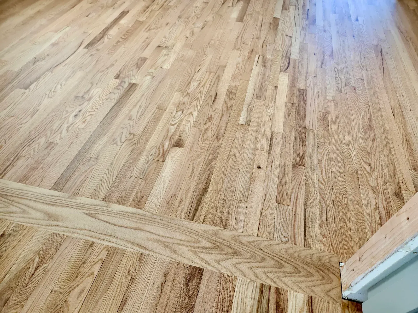 Light-colored hardwood flooring with varying grain patterns, and a wooden trim at the edge.