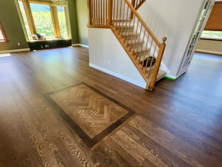 Wooden floor with parquet pattern, bordered by dark wood, and staircase in a home.