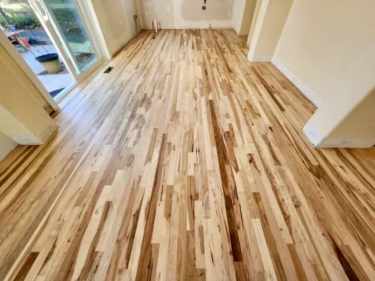 Light-colored hardwood floor in a room with white walls and a sliding glass door. Light-colored hardwood floor in a room with white walls and a sliding glass door.