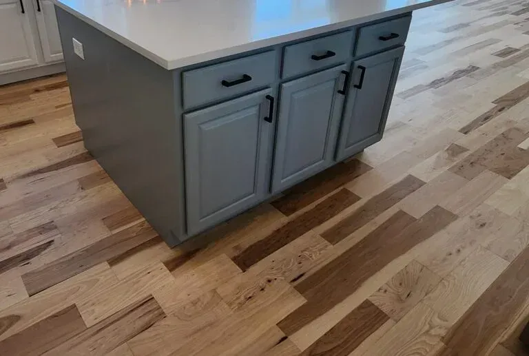 Kitchen island with gray cabinets, black hardware, and light countertop on wood floor.