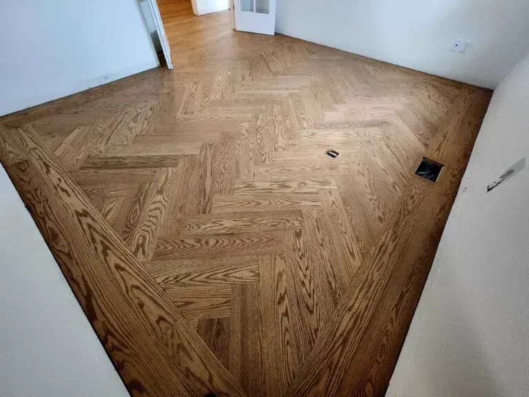 Herringbone pattern hardwood floor, stained medium brown, in a room with white walls.