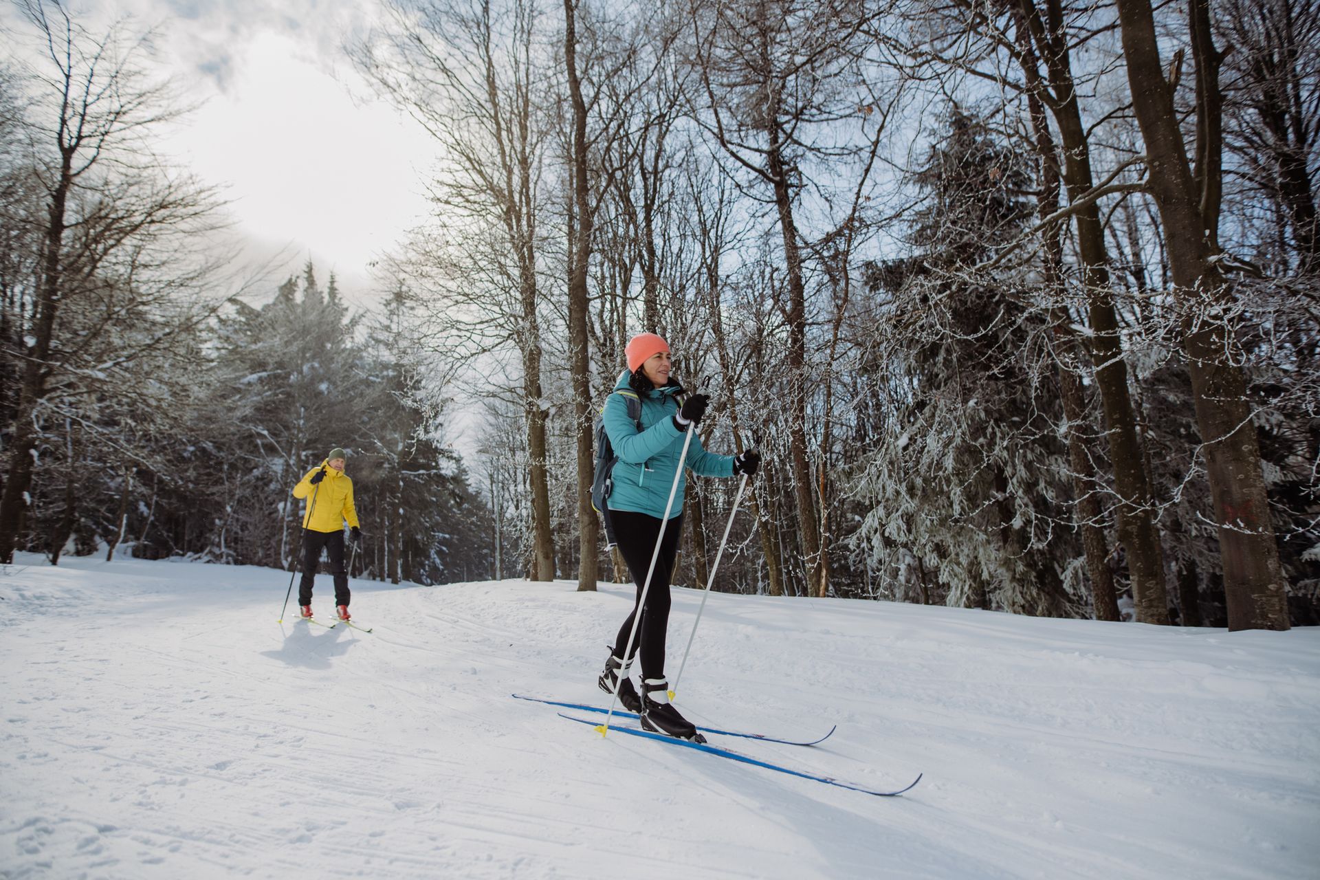 Couple cross-country skiing through a snowy forest trail in Wisconsin on a sunny winter day.