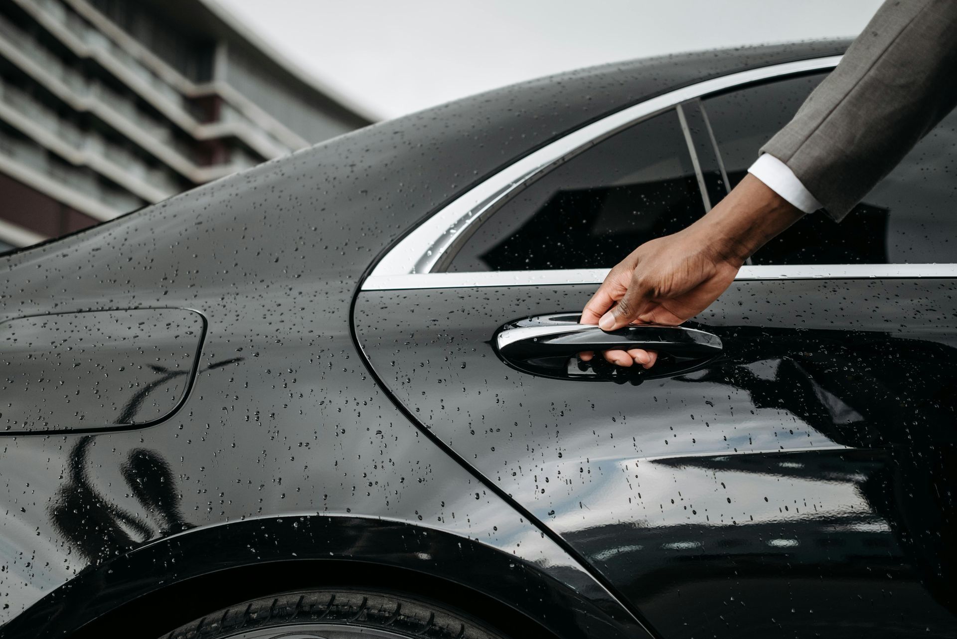 A man in a suit is opening the door of a black car.
