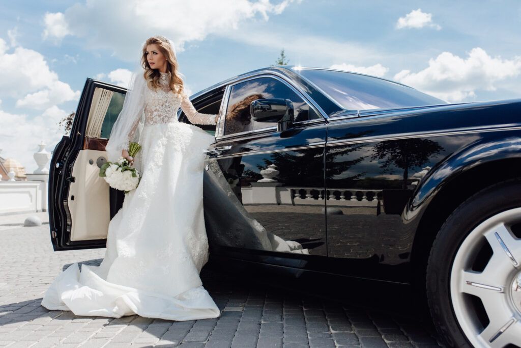 A bride in a wedding dress is getting out of a black limousine.