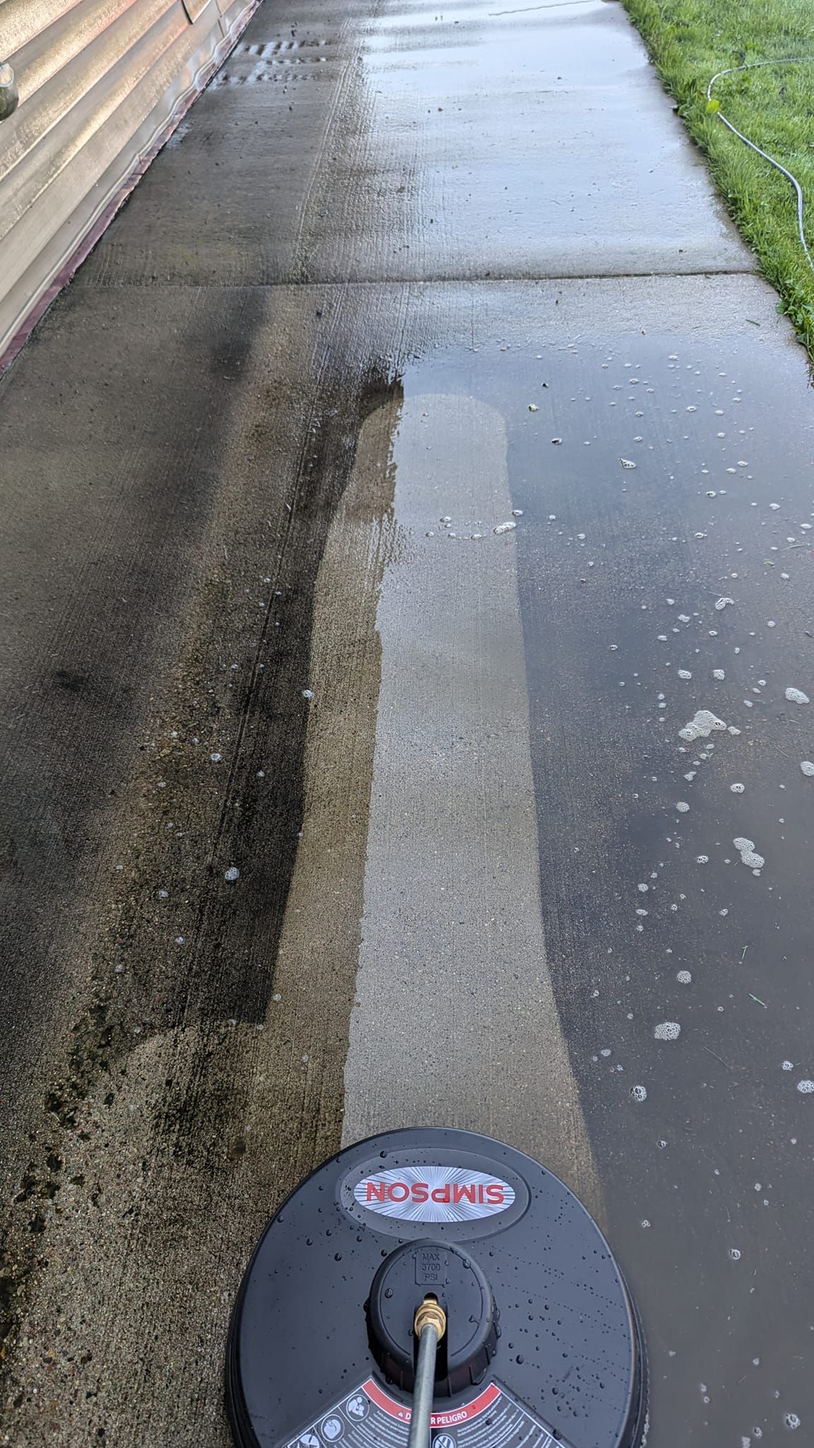 A concrete sidewalk is being cleaned with a pressure washer.