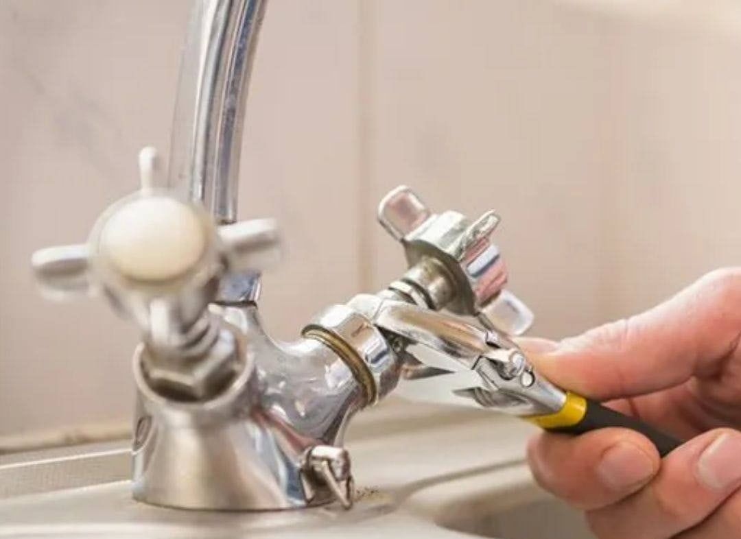 A Hand Using a Wrench to Tighten a Chrome Faucet in A Bathroom Setting — Malouf Plumbing In Pie Creek, QLD