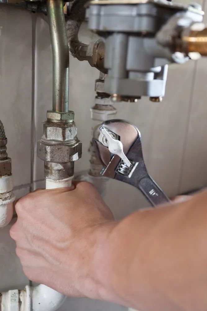 A Person Is Fixing A Pipe With A Wrench — Malouf Plumbing In Pie Creek, QLD
