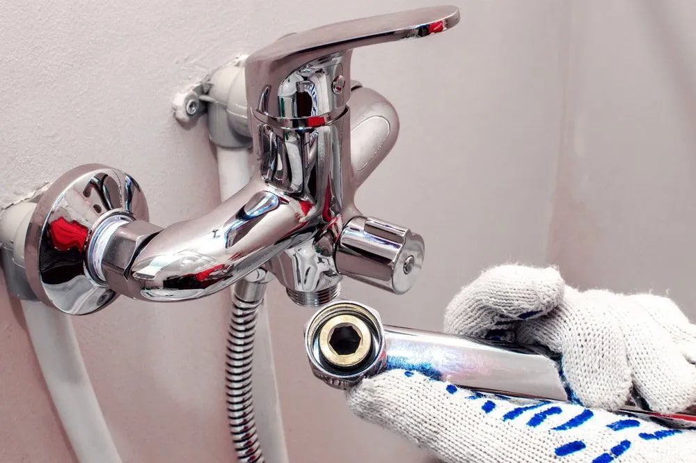 A person is fixing a bathroom faucet with a wrench — Malouf Plumbing In Pie Creek, QLD