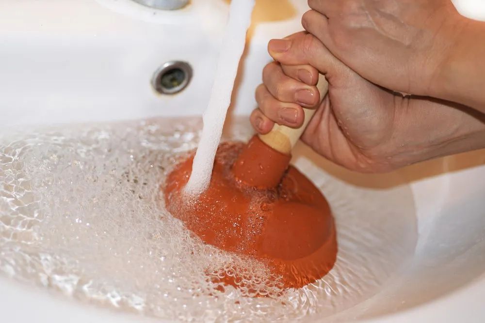 A Person Is Using A Plunger To Unblock A Sink — Malouf Plumbing In Pie Creek, QLD