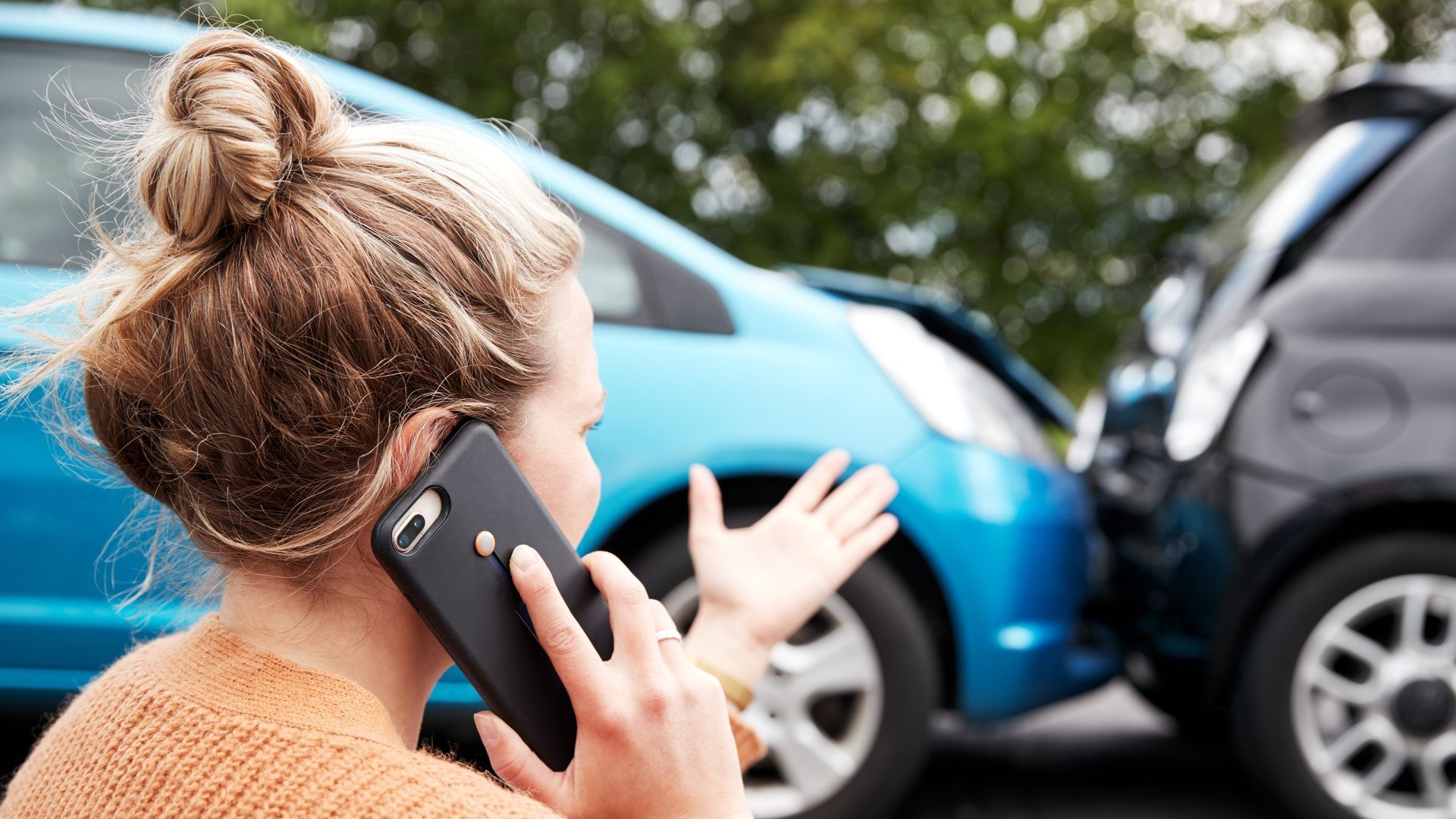 A woman is talking on a cell phone in front of a car accident.