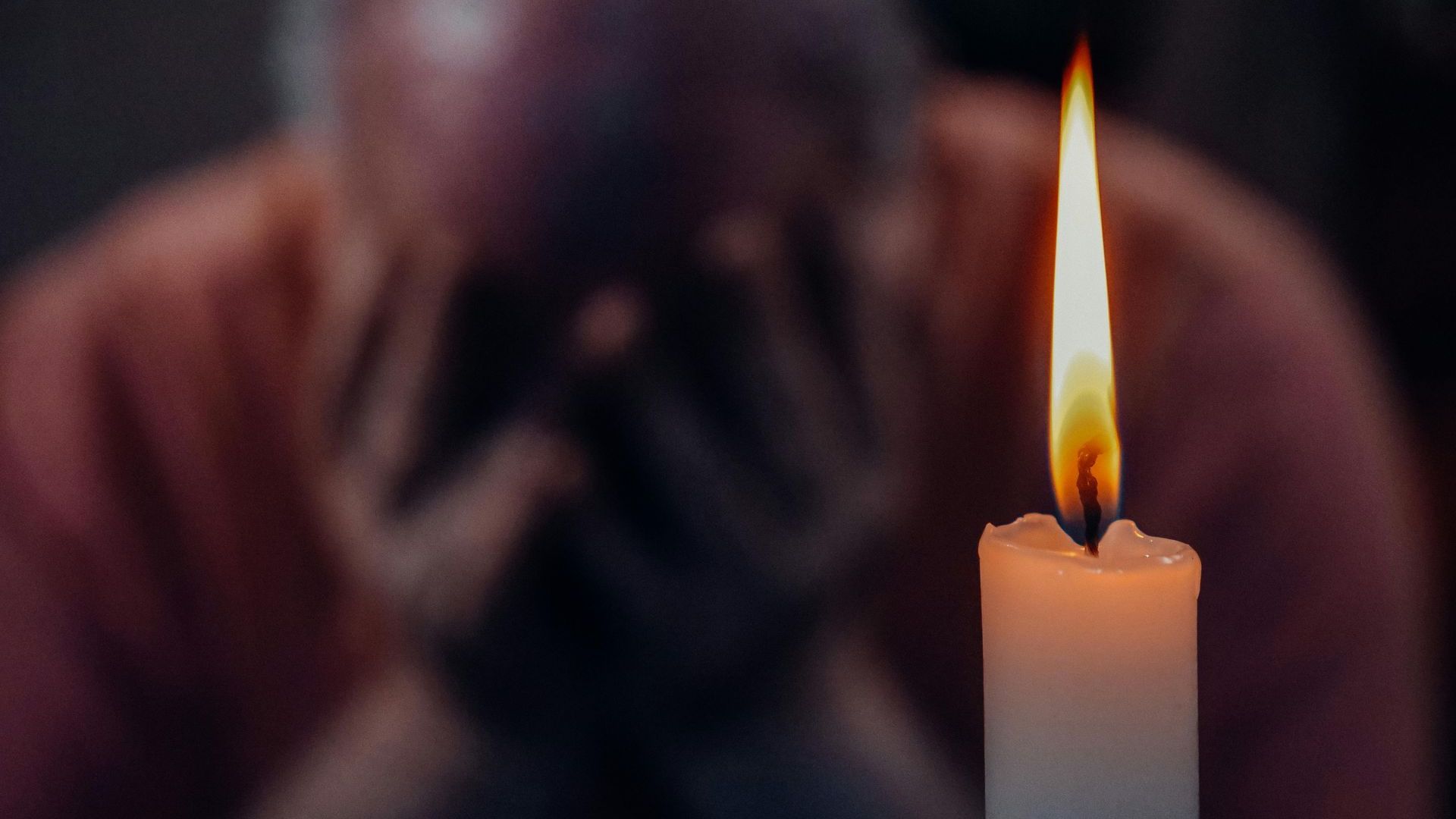 A man is praying in front of a lit candle.