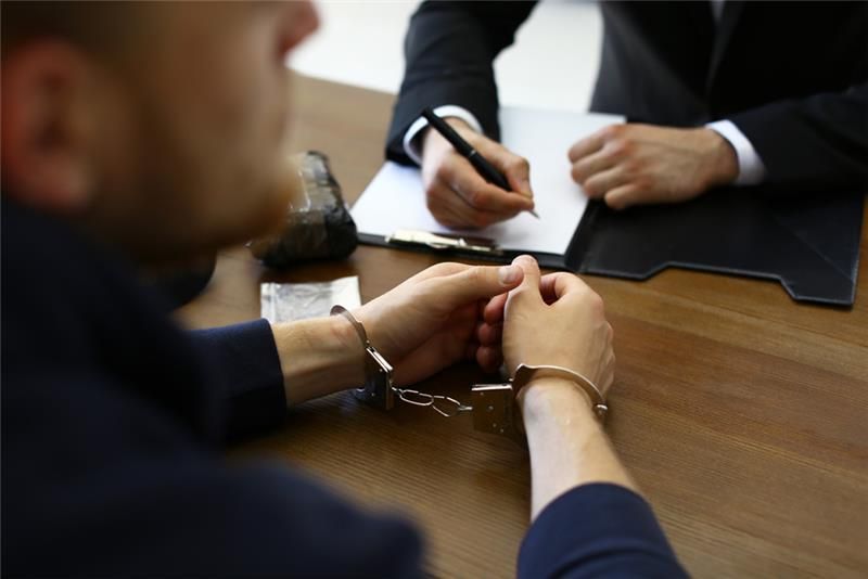 Defense attorney meeting with a handcuffed client during a legal consultation, discussing criminal