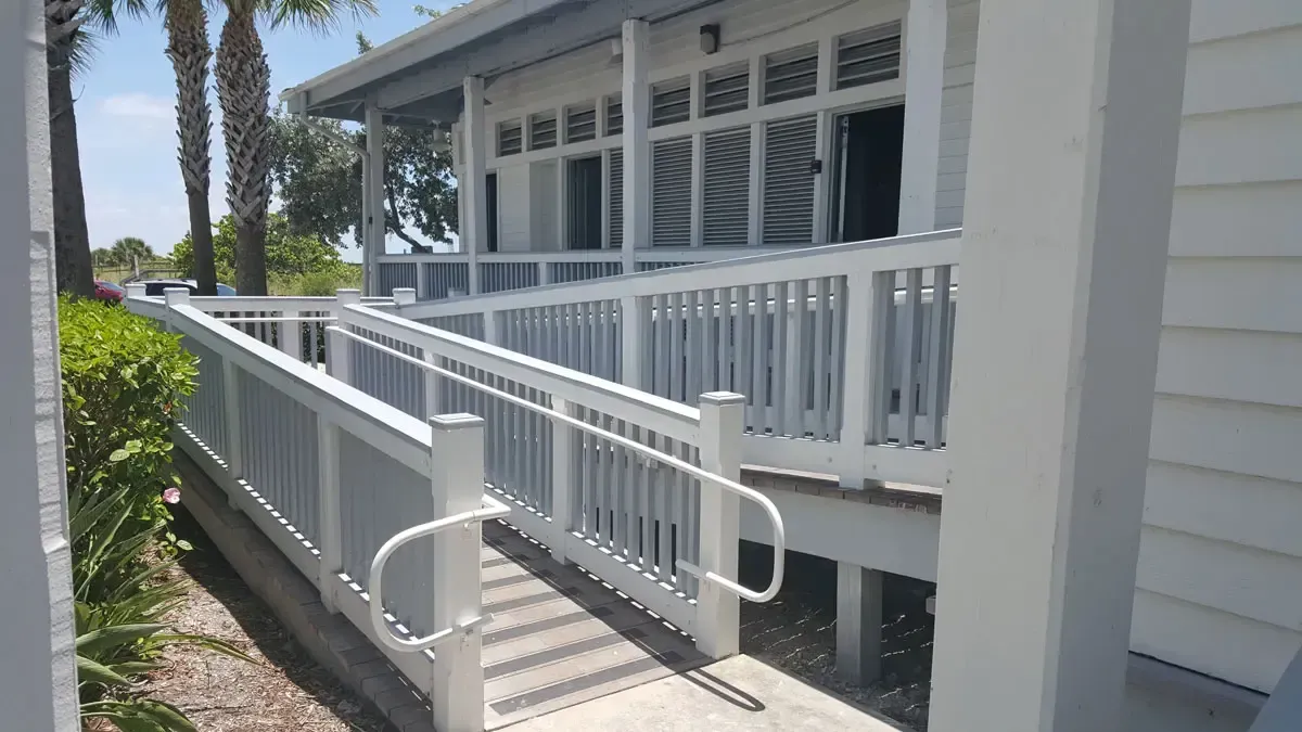 White ramp with handrails leading up to a building with windows and a covered porch.