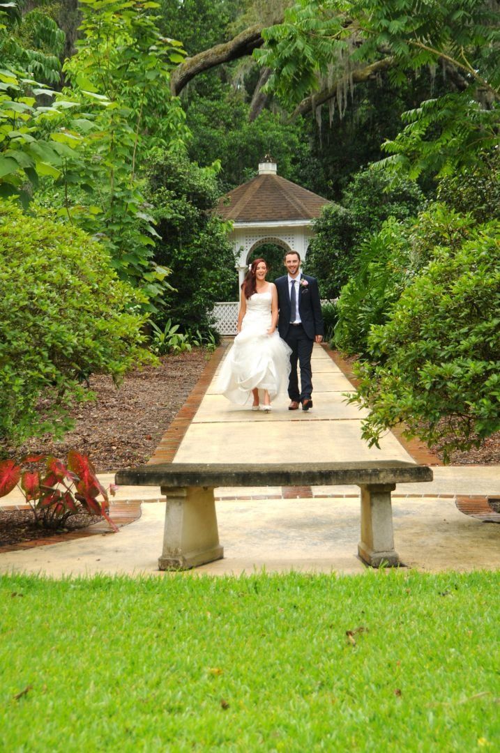Bride and groom walk a garden path toward a gazebo.