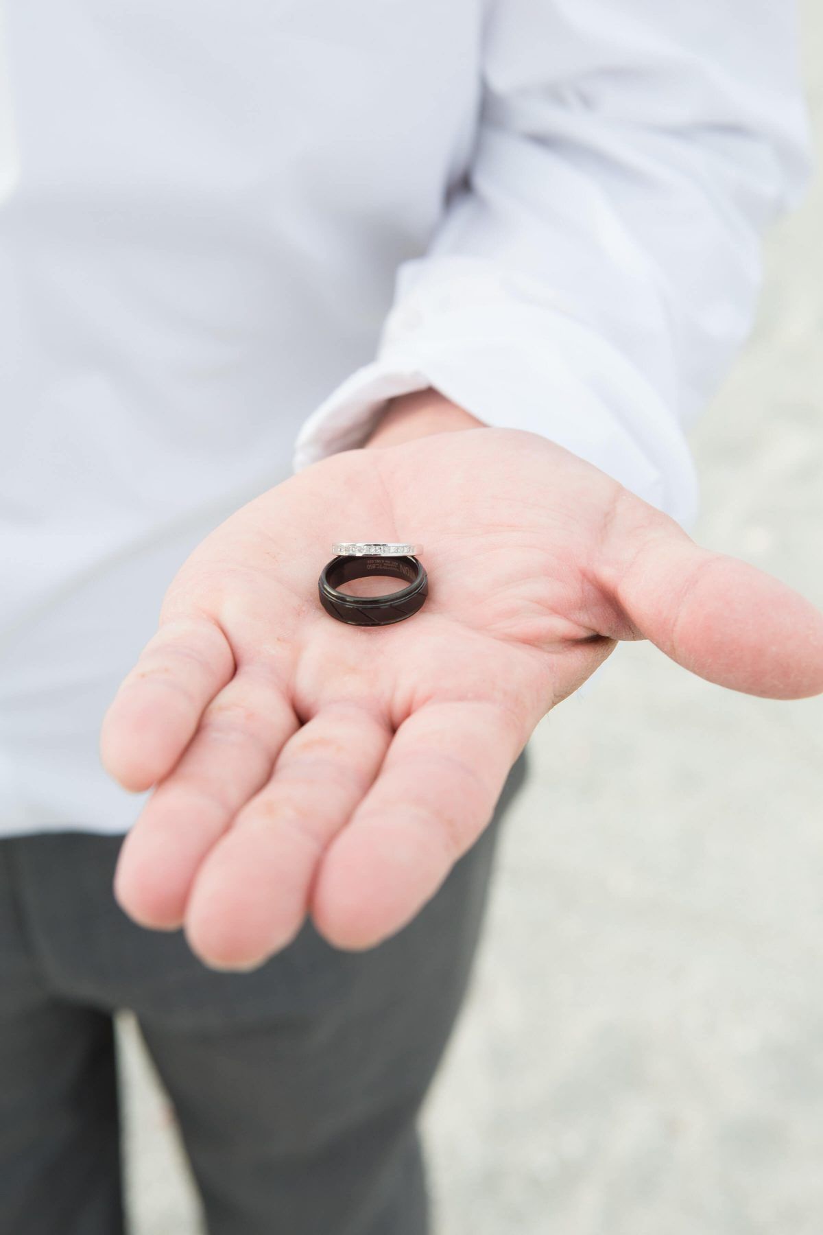 Person holding a dark ring in open palm, wearing a white shirt and gray pants.
