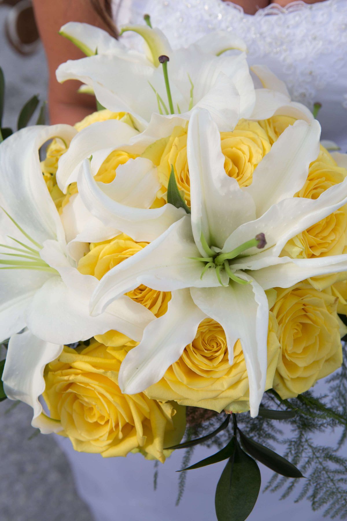 Bride holding a bouquet of white lilies and yellow roses.