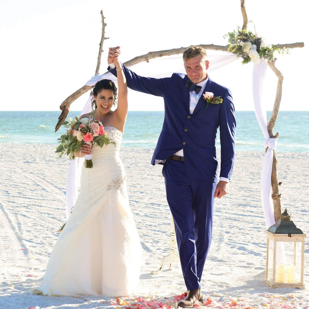 A bride and groom are walking on the beach at sunset.