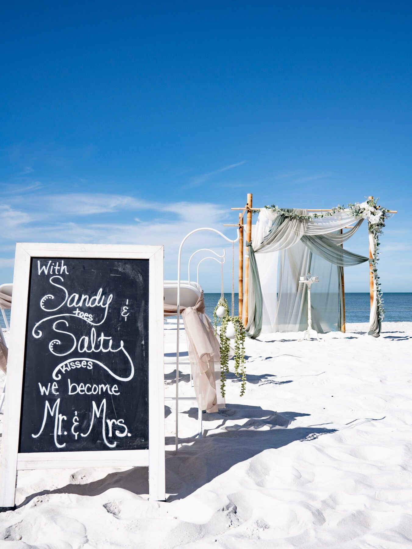 Beach wedding scene: Chalkboard sign reads 