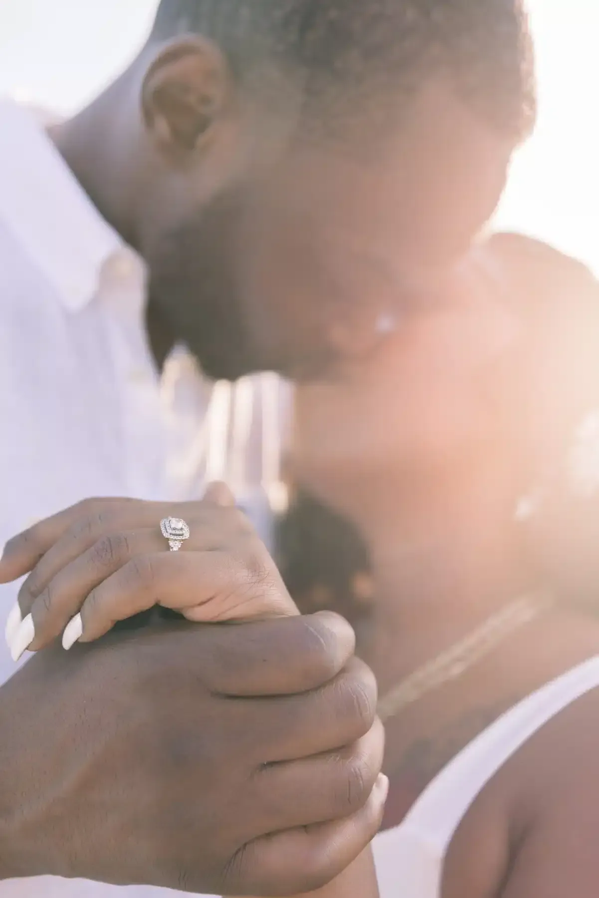 Couple embracing, sunlight highlights diamond ring on hand.