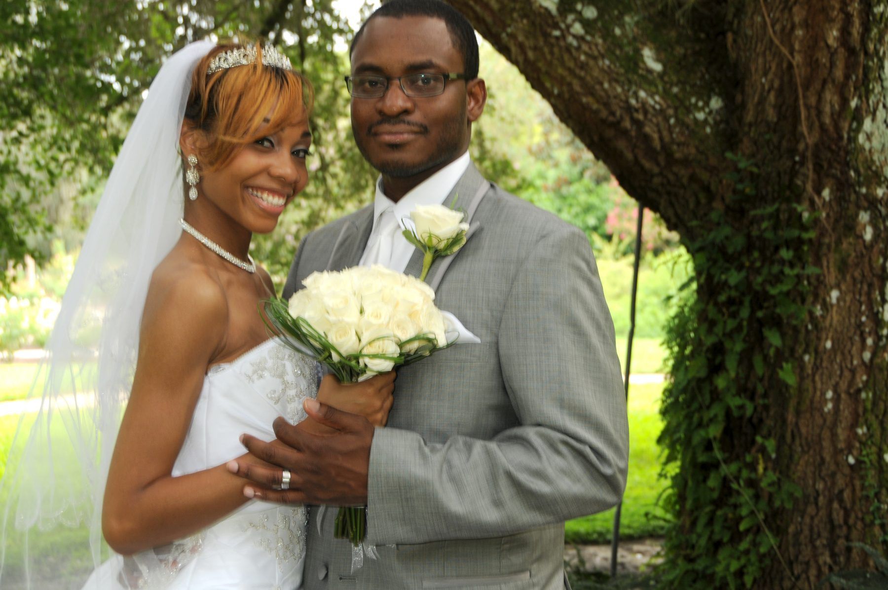 Bride and groom posing for a wedding photo outdoors. The bride is holding a bouquet and smiling, and the groom is smiling too.