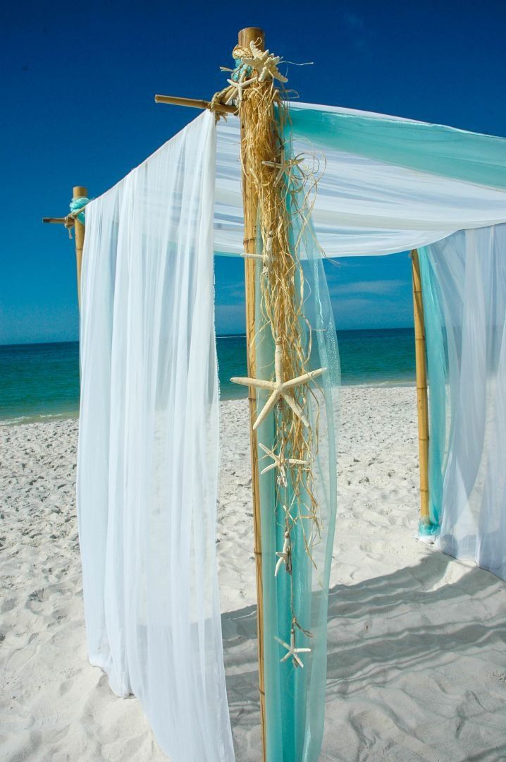Beach wedding canopy with white and teal fabric, decorated with starfish and natural elements, against a blue sky.