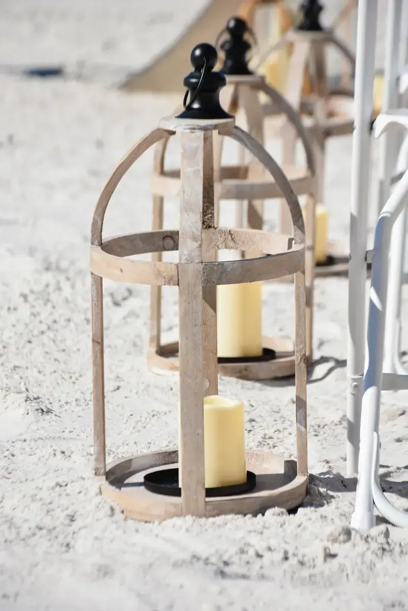 Wooden lanterns with candles on a sandy beach.