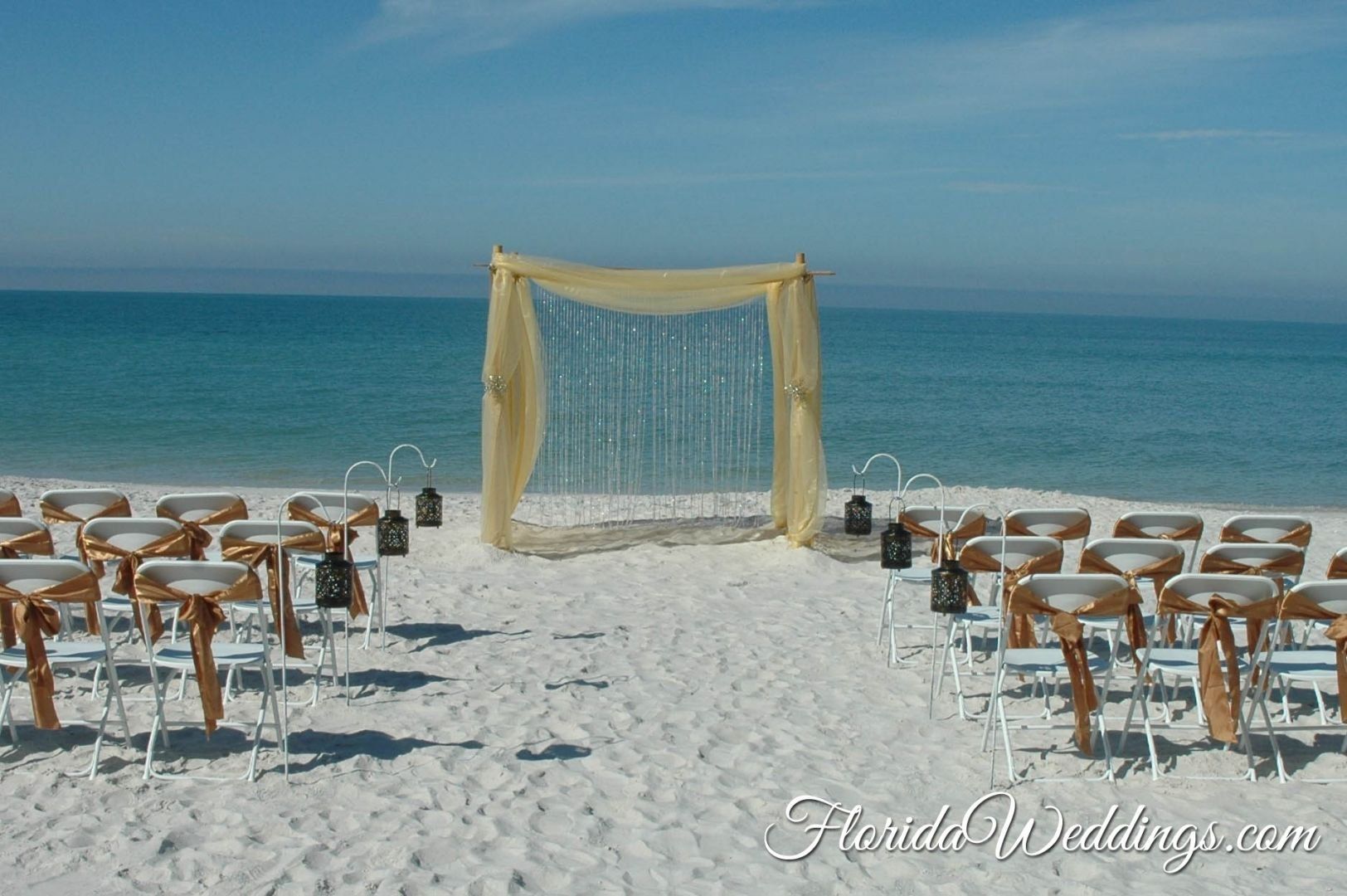 Beach wedding ceremony setup with chairs and draped arch.