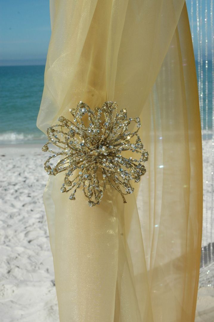 Beige fabric draped with a large, sparkly floral embellishment; beach and ocean in the background.