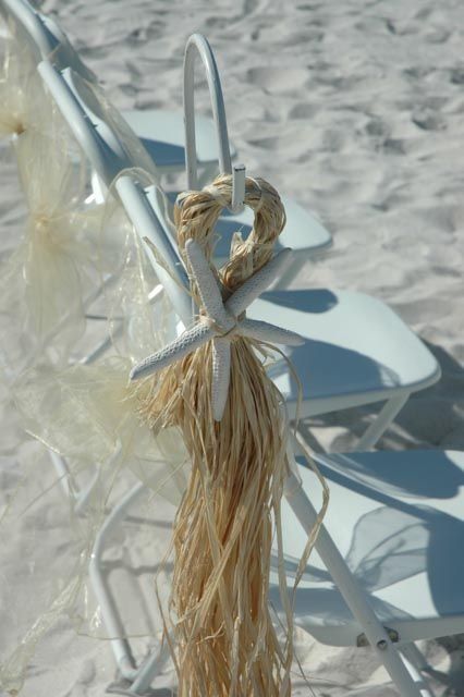 White chairs decorated with raffia and a starfish, on a sandy beach.