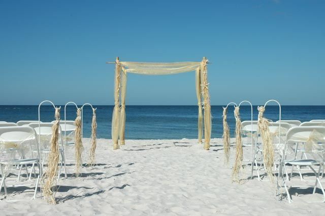 Beach wedding setup with white chairs, archway, and ocean view.