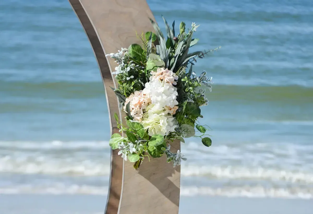 Beach wedding arch with floral arrangement, ocean background.