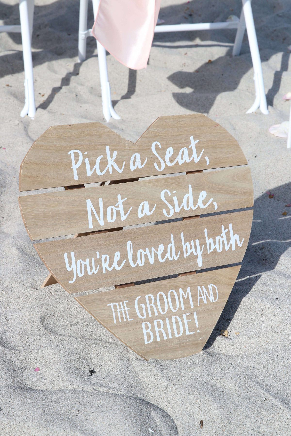 Heart-shaped wooden sign on a beach, saying 