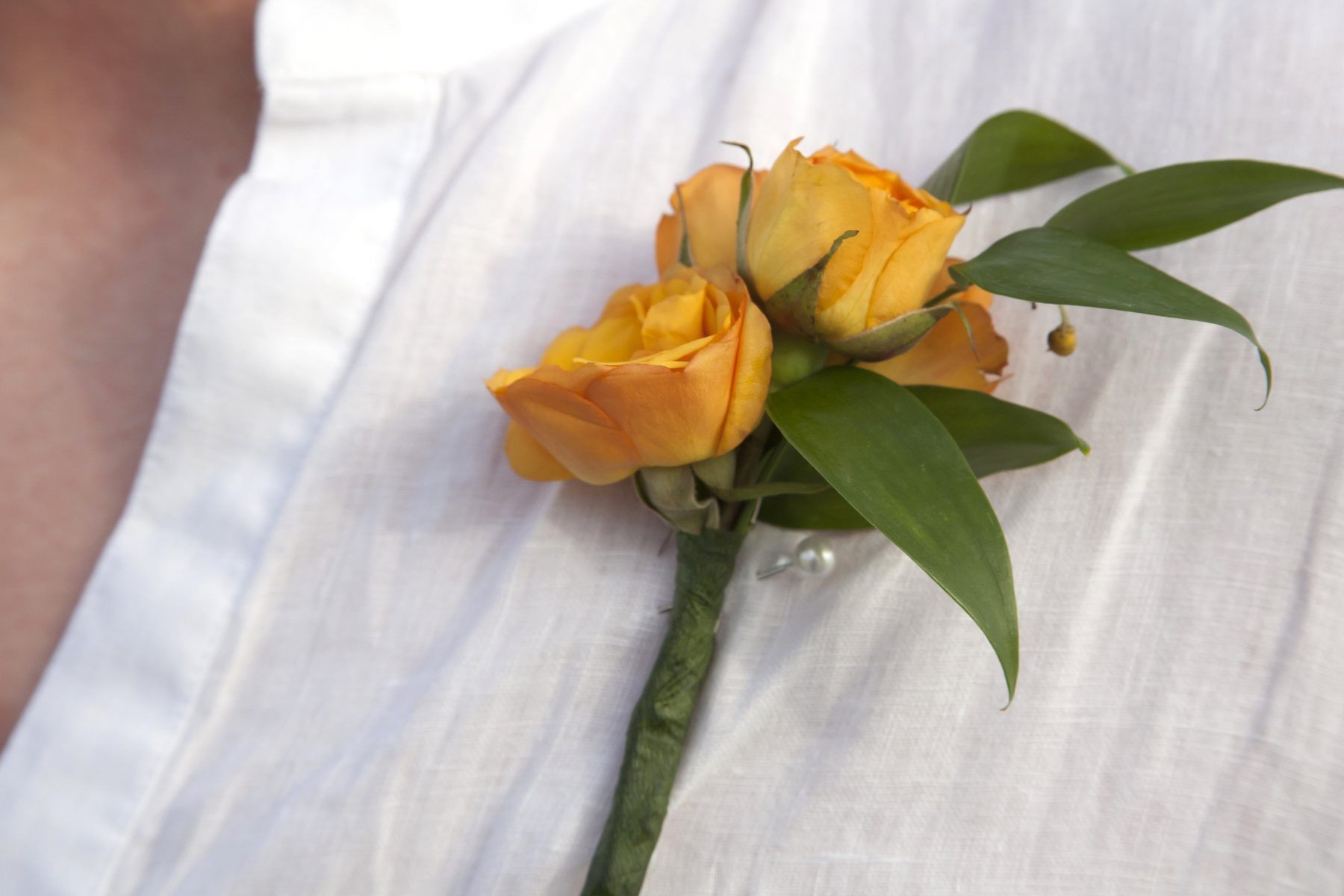 Yellow rose boutonniere pinned to a white shirt.