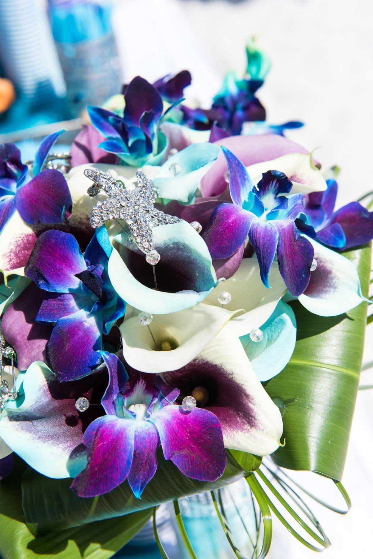 Purple and white floral bouquet with orchids, calla lilies, and a jeweled cross.